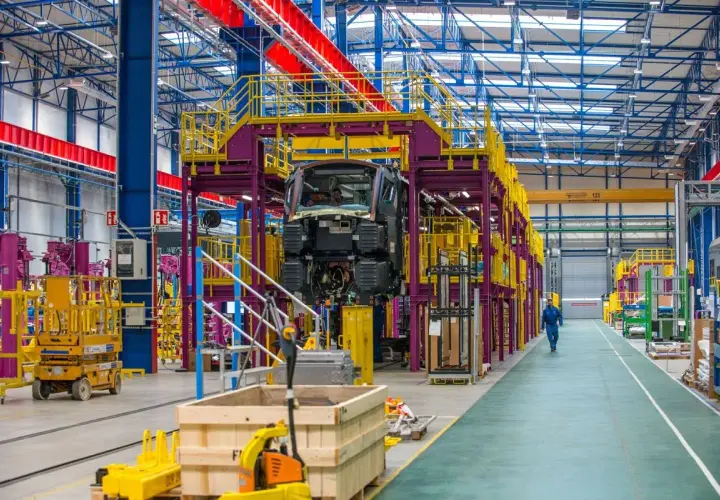 W hali produkcyjnej Alstom Konstal powstaje nowoczesny pociąg. Widać fragmenty konstrukcji, podnośniki i pracownika w niebieskim kombinezonie.
