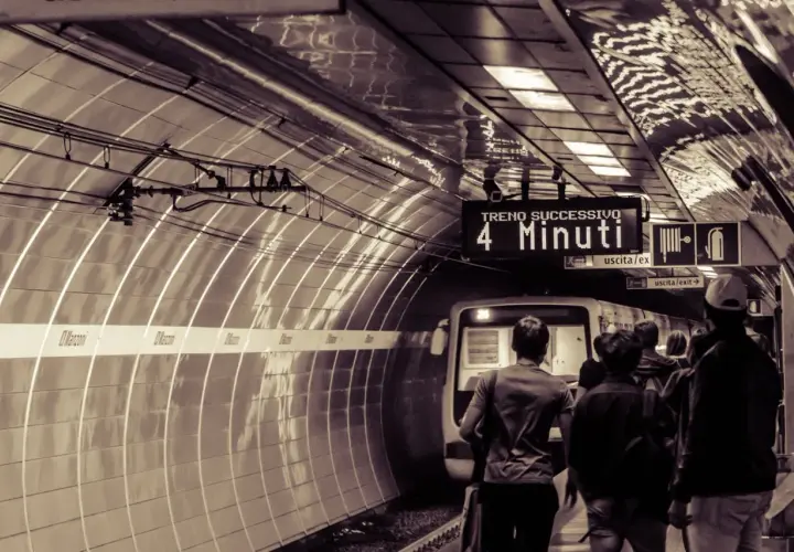 Persone attendono il treno sulla metro linea b. Un cartello indica "Treno successivo: 4 minuti".