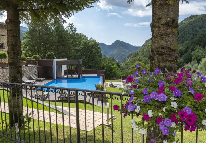 Un hotel de montaña con piscina azul, rodeado de vegetación. La coma i la pedra, un lugar de ensueño.