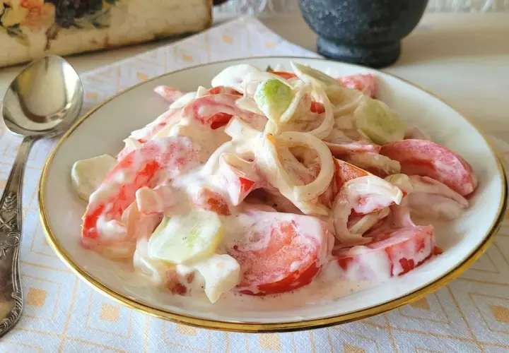 Pyszna sałatka pomidor ogórek cebula w kremowym sosie, podana na talerzu z ozdobną łyżką.