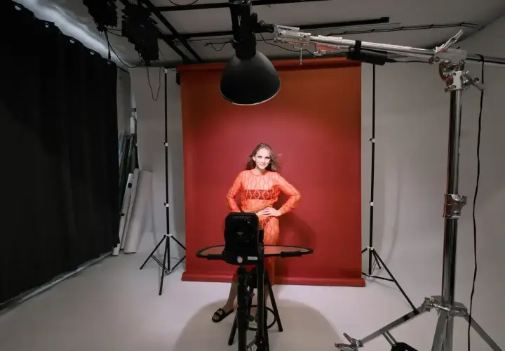 Profesjonalne oświetlenie studyjne przykłady: modelka pozuje na tle czerwonego tła, otoczona sprzętem fotograficznym i lampami.