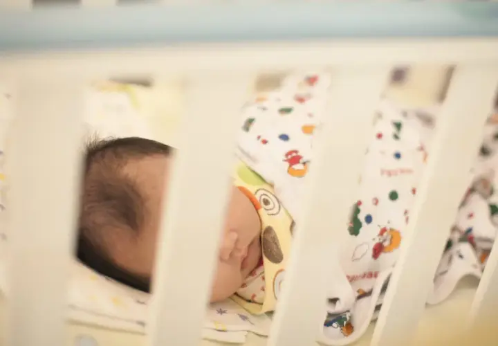 Malutki embrion, noworodek śpi w łóżeczku otulony kolorowymi kocykami z zabawnymi wzorami.