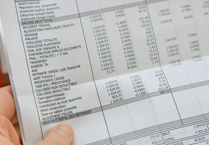 Une main tient une fiche de paie perdue, détaillant les salaires et les retenues.