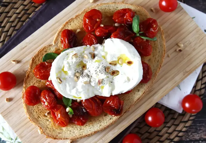 Pyszna bruschetta z burratą, pieczonymi pomidorkami koktajlowymi i orzeszkami pinii. Idealna na lekki posiłek.