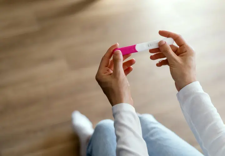 Dłonie trzymające test ciążowy, który może wskazać pierwsze objawy ciąży.