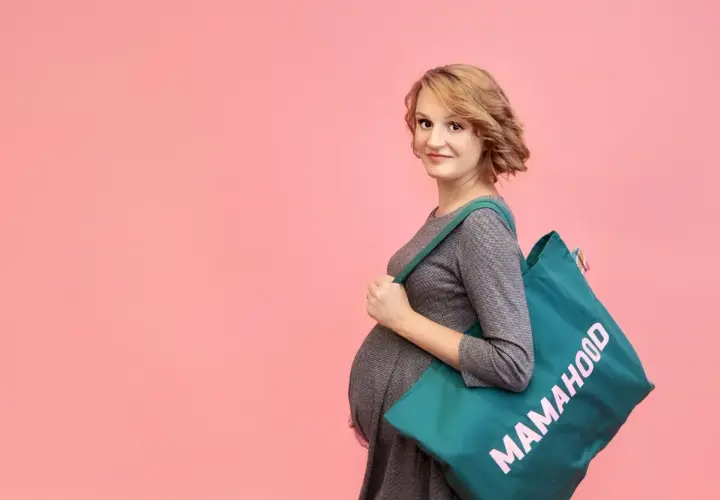 Przyszła mama z torbą "Mamahood" zastanawia się, kiedy spakować torbę do szpitala.