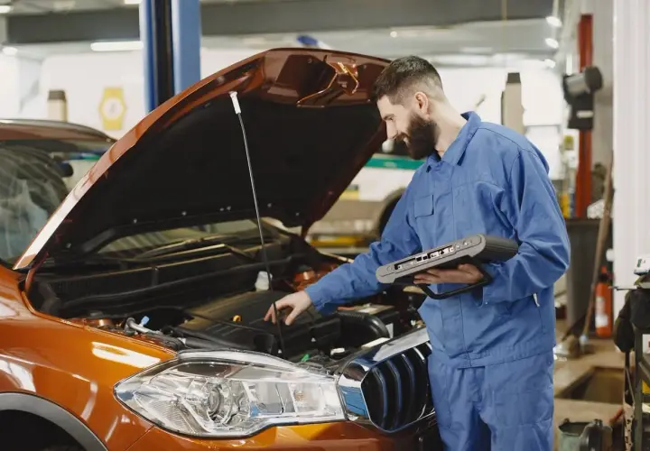 Mechanik z komputerem diagnostycznym sprawdza silnik. Zastanawiasz się, jak długo trwa wymiana oleju? To zależy od modelu auta i doświadczenia mechanika.