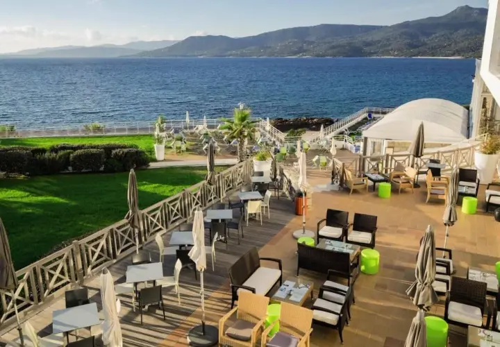 Terrasse d'un hôtel avec vue sur la mer, mobilier extérieur et verdure.