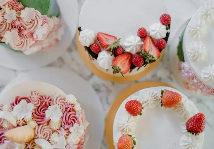 Flera vackra tårtor med fantasifulla dekorationer. En tårta är dekorerad med jordgubbar och maränger, en annan med rosa och vita blommor i frosting. Det är en festlig syn att dekorera tårta!