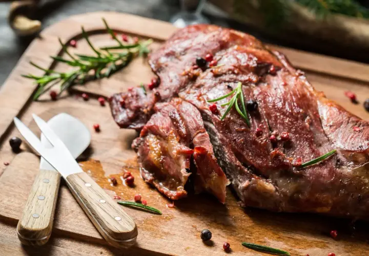 Soczysta dziczyzna, pieczona z rozmarynem i pieprzem, czeka na desce do krojenia. Obok leżą sztućce do mięsa.