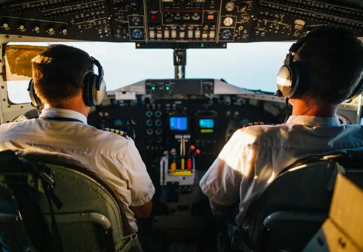 Dwóch pilotów samolotu w słuchawkach na tle kokpitu.