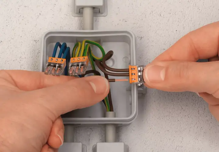 Mains électriques connectées dans une boîte encastrée. Le diamètre de la boîte encastrement permet d'accueillir les fils et les connecteurs.