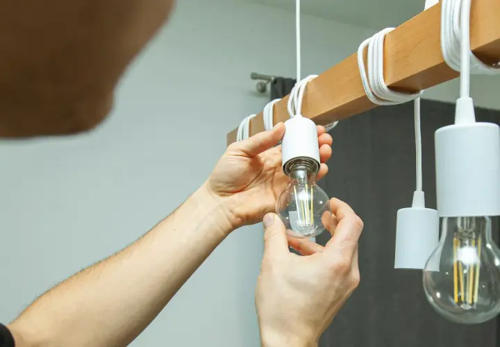 Ręce wkręcają żarówkę LED do drewnianego elementu lampy. Czy ledy się nagrzewają? Ta żarówka wygląda na chłodną.