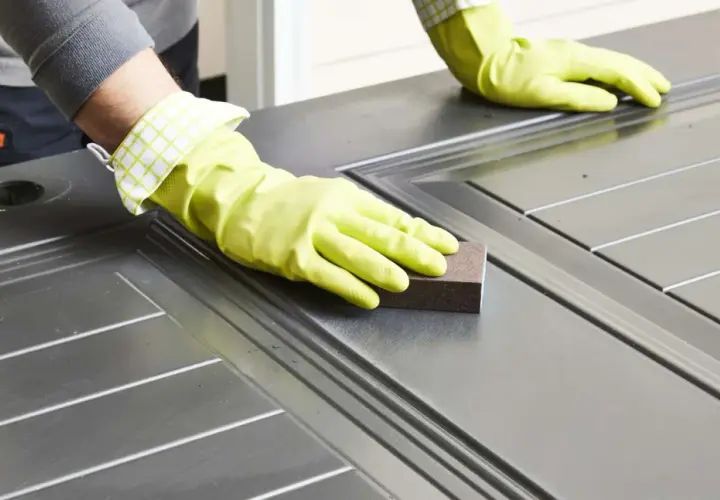 Manos enguantadas lijando una puerta para pintar aluminio.