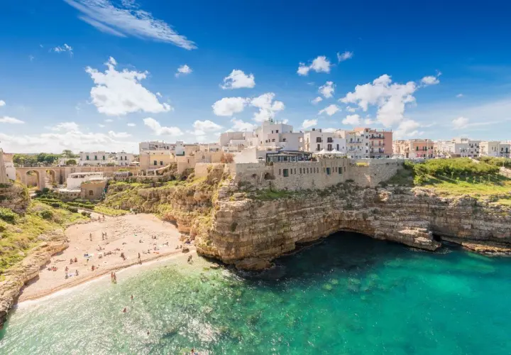 Vue panoramique de la plage de Polignano a Mare, avec ses falaises rocheuses, ses eaux turquoise et ses maisons blanches perchées.