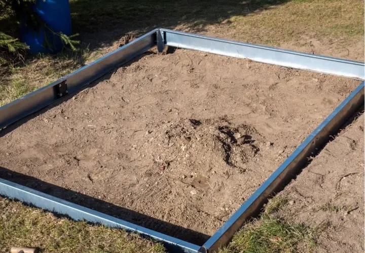 Metalowa rama na ziemi, gotowa na zrobienie fundamentu pod szklarnię.