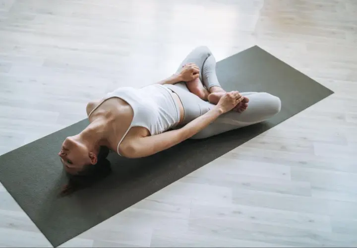 Kobieta w pozycji supta baddha konasana na macie do jogi, relaksująca biodra i pachwiny.