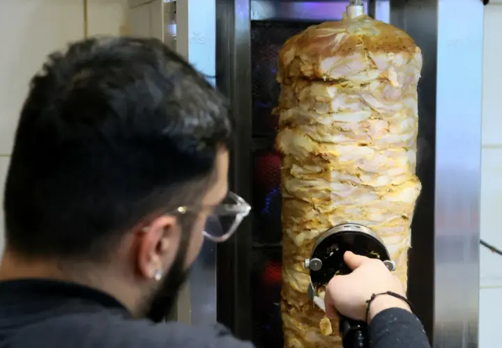 Mężczyzna kroi mięso z pionowego rożna na kebab.