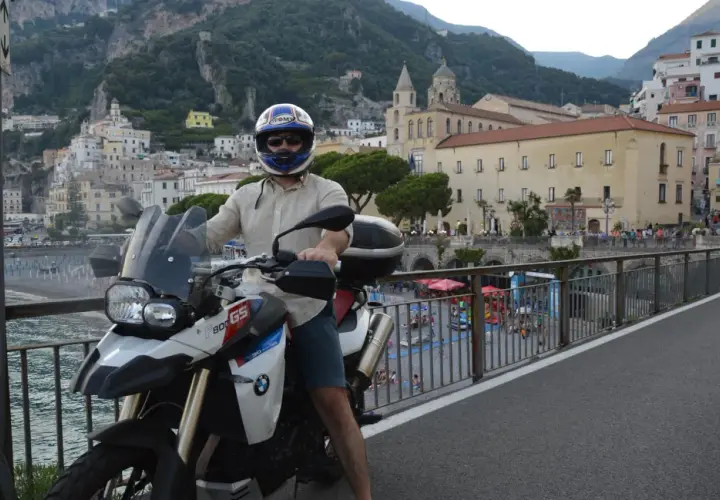 Motociclista in sella alla sua BMW, ammira il panorama della meta costiera amalfitana con le case aggrappate alla montagna.
