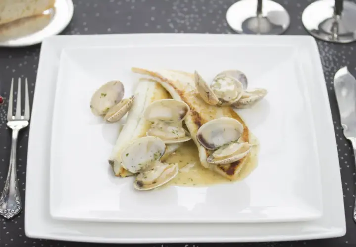Coruxo pescado con almejas en salsa cremosa, servido en plato blanco.