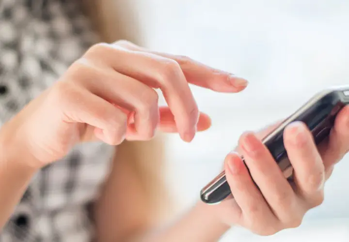 Dłonie obsługują smartfon, palce przesuwają się po ekranie, jakby wybierały opcję z menu +20 kierunkowego.