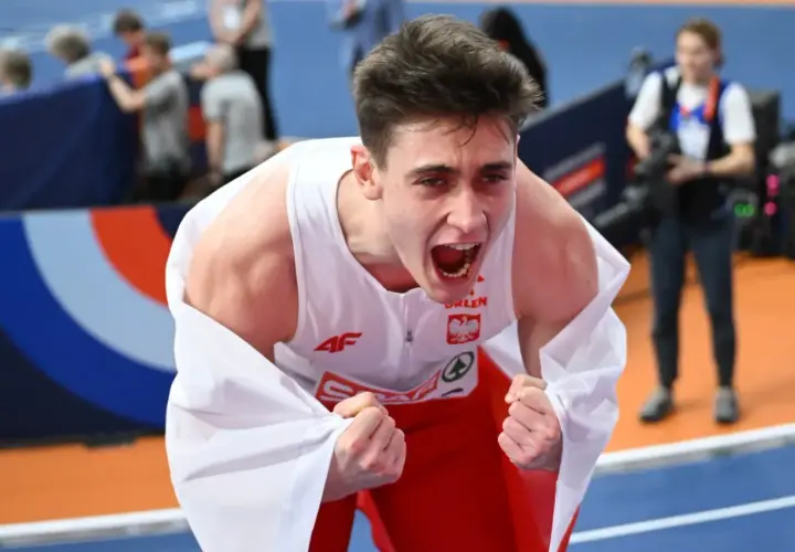 Młody lekkoatleta w biało-czerwonej koszulce okryty białą flagą, krzyczy z radości po zwycięstwie na halowych mistrzostwach europy lekkoatletyka.