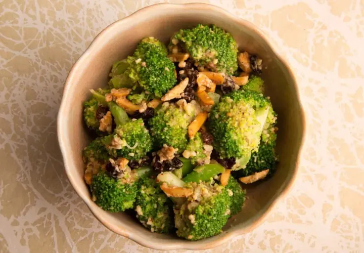 Ensalada de brócoli fresca con pasas y nueces, servida en un cuenco de cerámica.