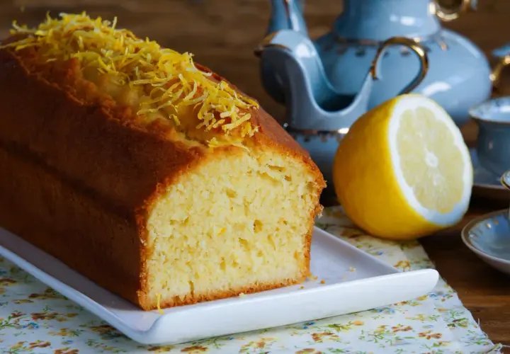 Puszysta babka cytrynowa, ozdobiona skórką cytrynową, czeka na herbatę z błękitnego serwisu.