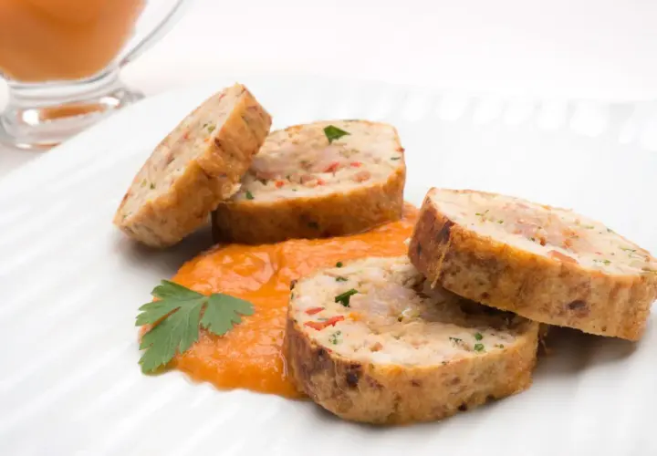Rollo de bonito cortado en rodajas, servido sobre puré de pimientos y decorado con perejil.