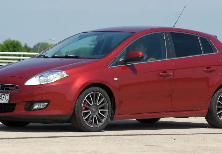 Czerwony Fiat Bravo z kierowcą za kierownicą, zaparkowany na zewnątrz.