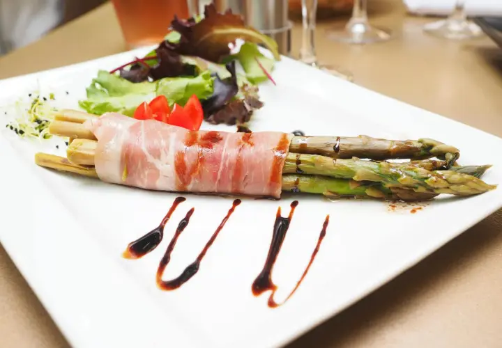 Zielone szparagi owinięte szynką parmeńską, podane z sałatką i sosem balsamicznym.