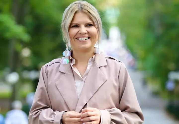 Uśmiechnięta Marta Manowska w beżowym płaszczu i efektownych kolczykach, jakby właśnie spotkała swojego partnera.