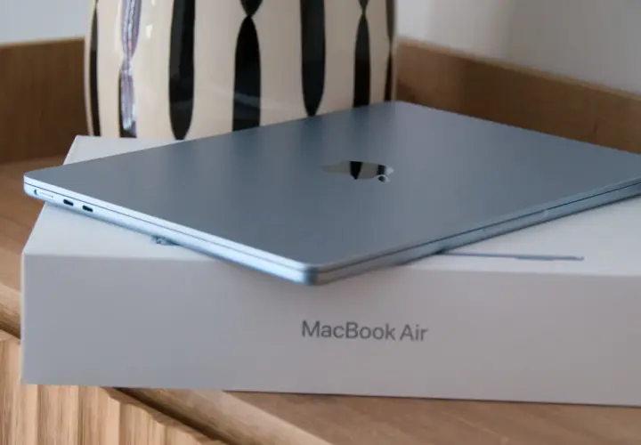 MacBook Air azul cerrado sobre su caja, con un jarrón al fondo.