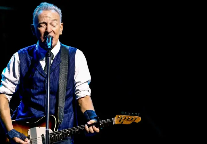 Bruce Springsteen z gitarą na scenie, w niebieskiej kamizelce i białej koszuli. Niezapomniane koncerty legendy rocka.