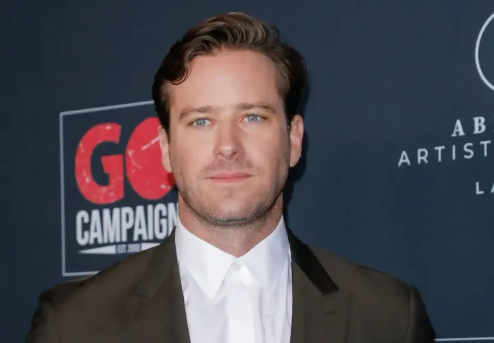 Armie Hammer, med sina blå ögon och mörk kostym, poserar framför en bakgrund med texten "GO CAMPAIGN".