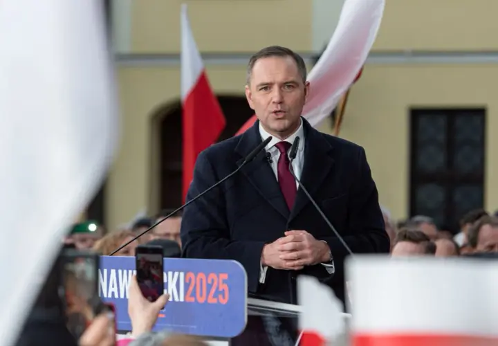 Polityk przemawia na tle flag. Na banerze widnieje napis "NAWROCKI 2025".