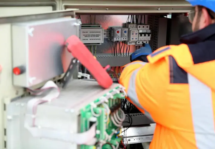 Elektryk w pomarańczowej kamizelce pracuje przy panelu sterowania, podłączając kabel neutralny.
