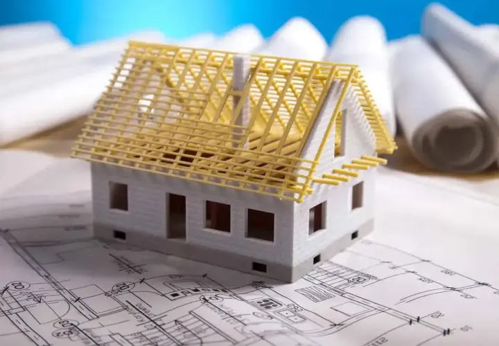 Model domu na planach architektonicznych, z widoczną konstrukcją dachu. Zastanawiasz się, ile kosztuje adaptacja projektu?