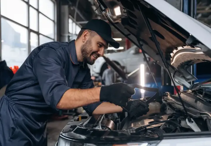 Uśmiechnięty mechanik w granatowym kombinezonie sprawdza silnik. Zastanawiasz się, ile zarabia mechanik?