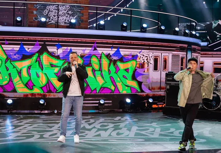 Raperzy na scenie, w tle graffiti na wagonie metra. To scena z koncertu, gdzie brzmią **paktofonika utwory**.