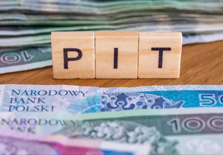 Drewniane klocki z literami "PIT" na tle polskich banknotów. To symbol ulgi na dzieci, która może pomóc w rozliczeniu podatkowym.
