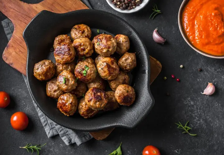 Polpette dorate e succulente, cotte alla perfezione nella friggitrice ad aria, pronte per essere gustate con salsa e pomodorini freschi.