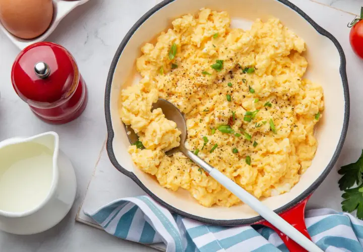 Oeufs brouillés crémeux, parsemés de ciboule fraîche et de poivre noir, servis dans une poêle rouge. Un délice pour le petit-déjeuner.