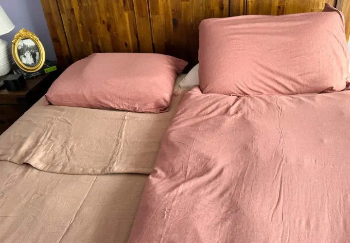 A bedspread can be used as a blanket, as shown by this cozy, pink-covered bed with a wooden headboard.