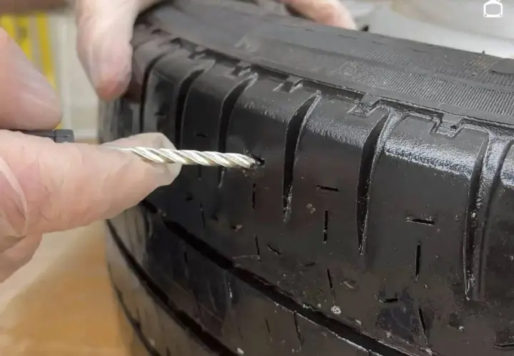 Manos con guantes reparando un pinchazo en un neumático con una herramienta.