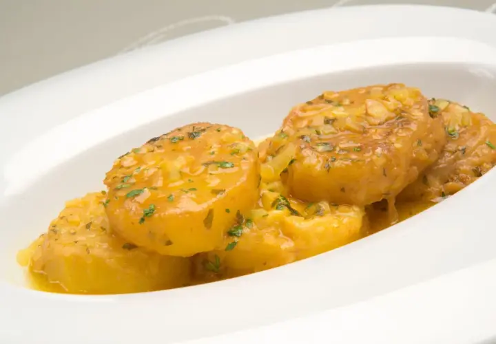 Patatas a la importancia, doradas y jugosas, bañadas en una salsa con ajo y perejil, servidas en un plato blanco.