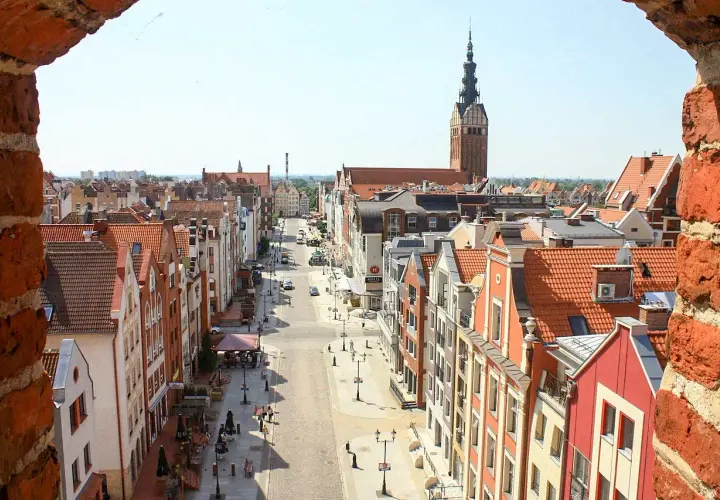 Widok na ulicę Starego Miasta w Elblągu z charakterystyczną wieżą kościoła. Urokliwe kamienice i brukowana droga tworzą piękne elbląg atrakcje.