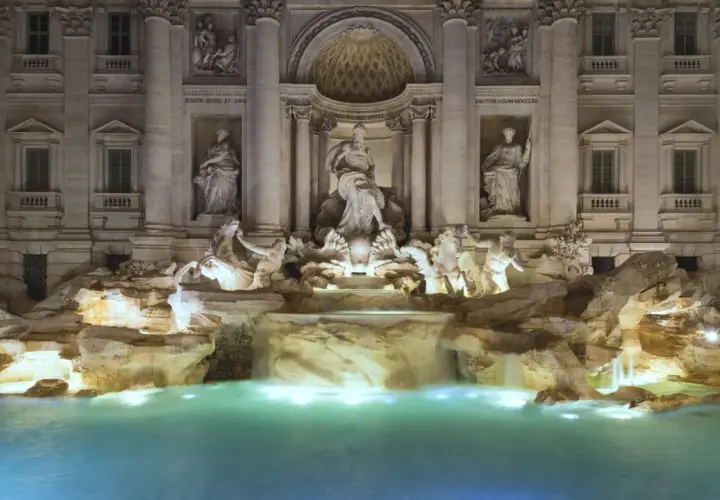 Fontana di Trevi stile barocco, con statue di divinità marine e cavalli marini che emergono da rocce e cascate, illuminata di notte.