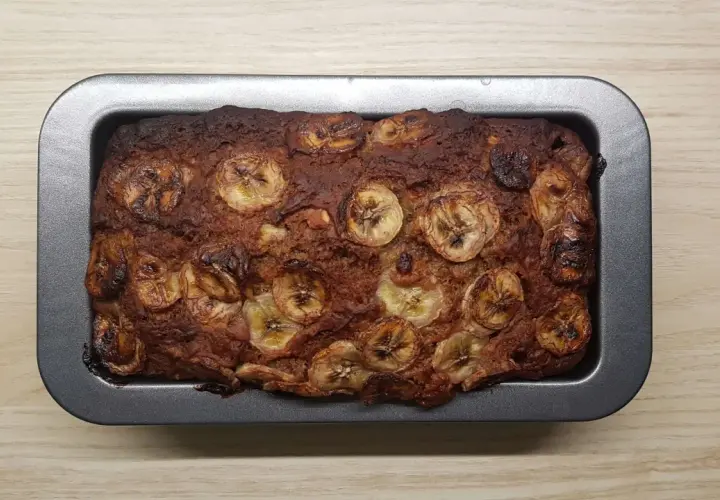 Upieczony proteinowy chlebek bananowy z plasterkami banana na wierzchu, w metalowej formie.