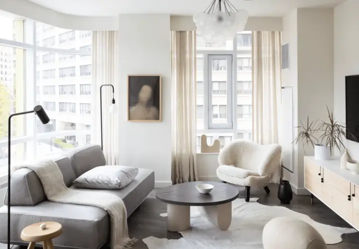 A cozy living room, perfect for learning how to furnish a small apartment. A grey sofa, fluffy armchair, and round coffee table create a welcoming space.
